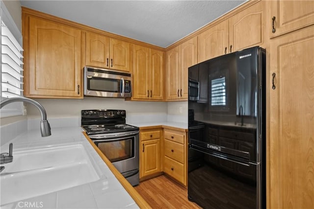 kitchen featuring a sink, stainless steel appliances, light countertops, a textured ceiling, and light wood-type flooring