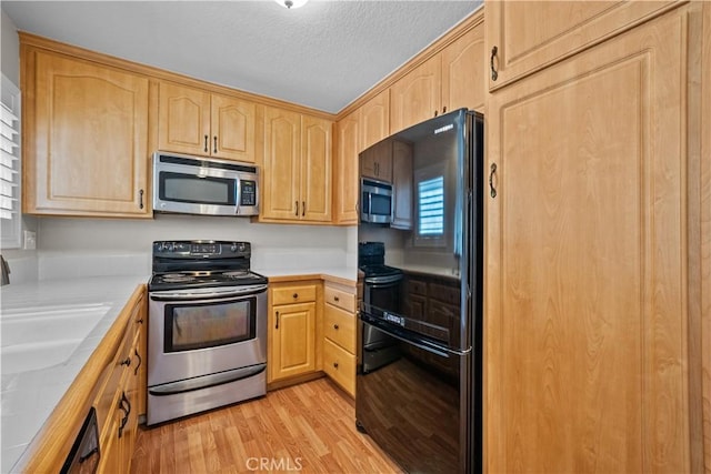 kitchen featuring light wood-type flooring, light brown cabinets, a sink, a textured ceiling, and appliances with stainless steel finishes