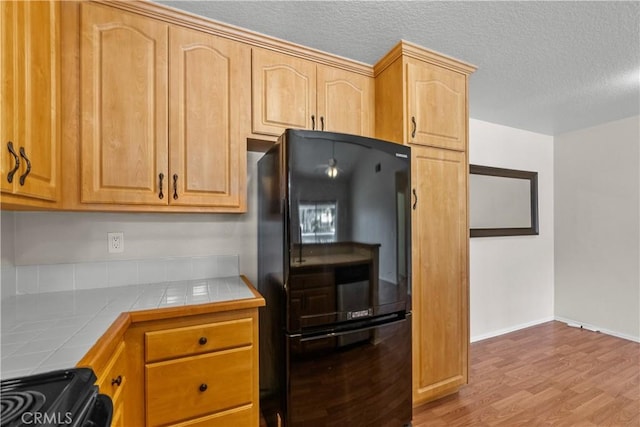 kitchen featuring freestanding refrigerator, tile counters, stove, a textured ceiling, and light wood-type flooring