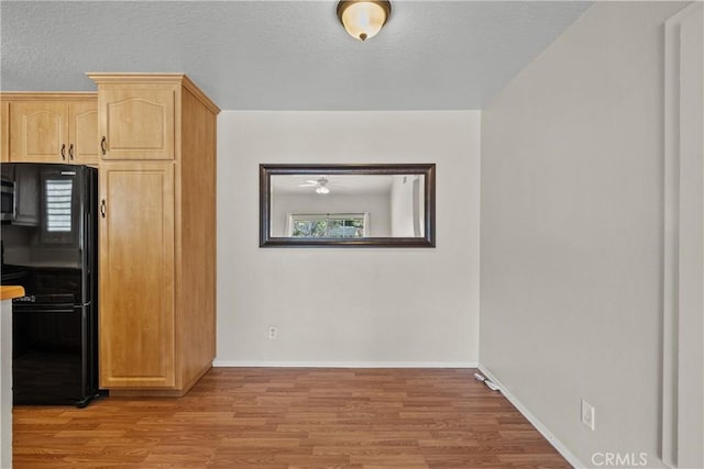 kitchen with light wood-type flooring, a textured ceiling, light brown cabinets, and freestanding refrigerator