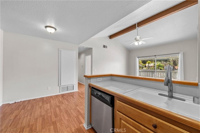 kitchen featuring visible vents, a sink, tile countertops, dishwasher, and vaulted ceiling with beams