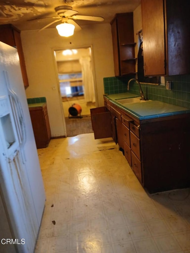 kitchen with tile countertops, white fridge with ice dispenser, light floors, and a sink