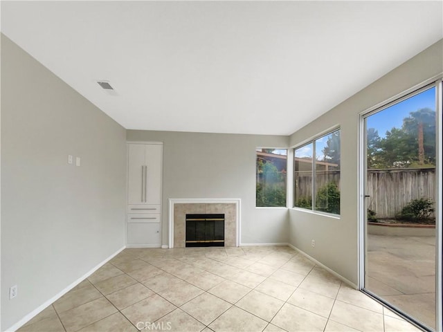 unfurnished living room featuring a tiled fireplace, light tile patterned floors, visible vents, and baseboards