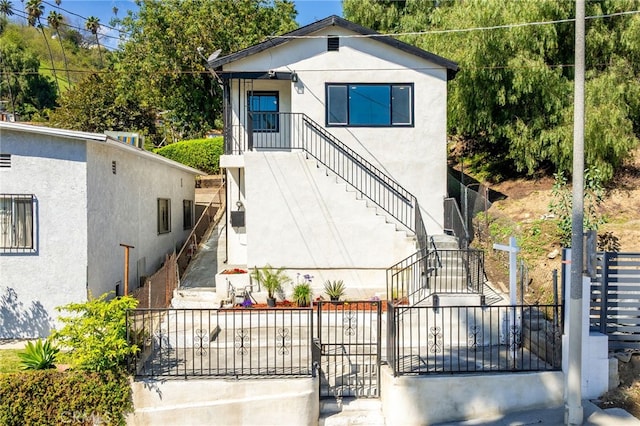 view of front of home featuring stucco siding, stairs, and fence