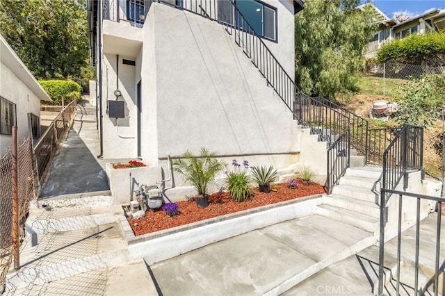 view of side of property featuring stairway, fence, and stucco siding