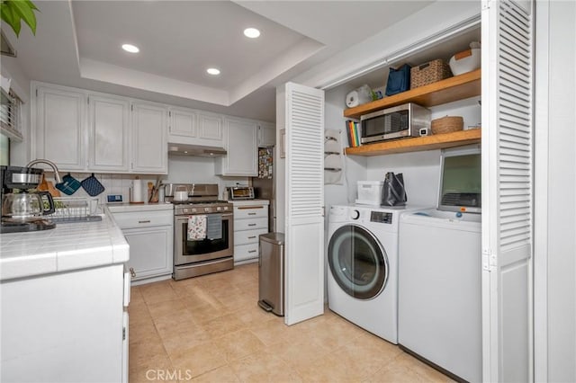 kitchen with a raised ceiling, under cabinet range hood, independent washer and dryer, recessed lighting, and stainless steel appliances