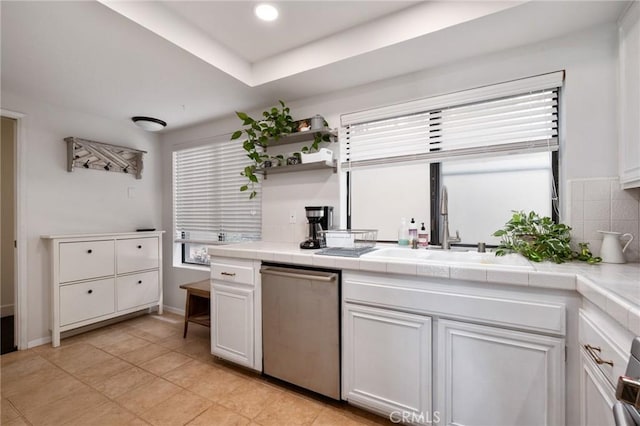 kitchen with tile countertops, white cabinetry, light tile patterned flooring, dishwasher, and a sink