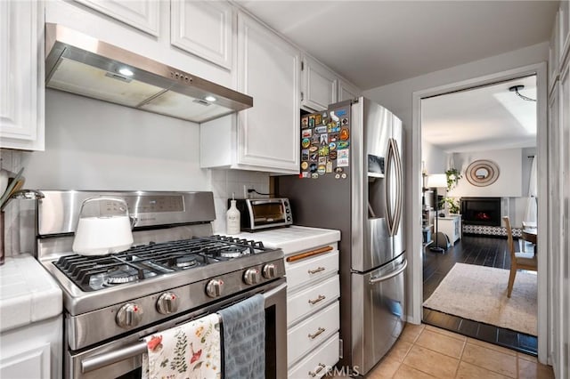 kitchen featuring tasteful backsplash, white cabinetry, under cabinet range hood, stainless steel appliances, and tile countertops