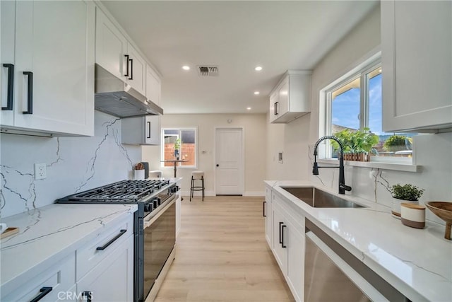 kitchen featuring visible vents, a sink, under cabinet range hood, stainless steel appliances, and light wood-style flooring