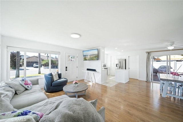 living area featuring plenty of natural light, ceiling fan, light wood-type flooring, and baseboards