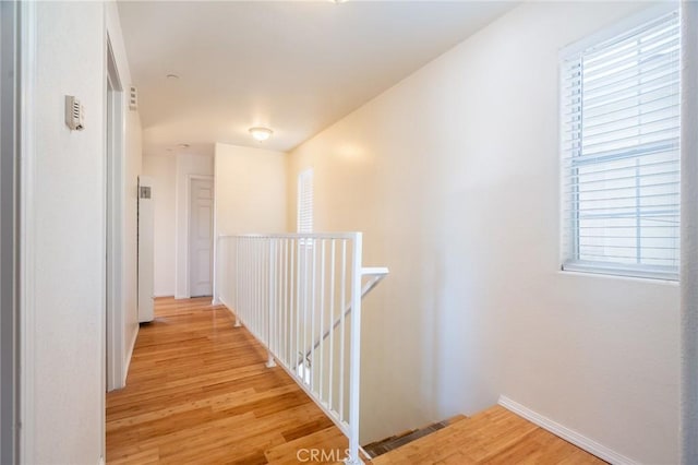 hallway with baseboards, an upstairs landing, light wood-style floors, and visible vents