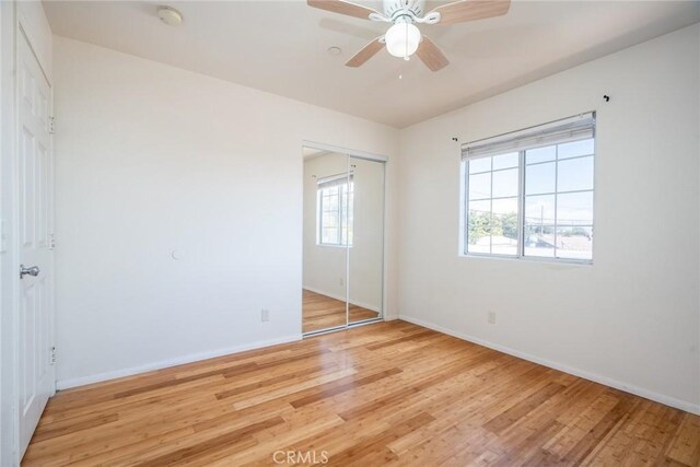 unfurnished bedroom featuring a closet, baseboards, light wood-style floors, and a ceiling fan