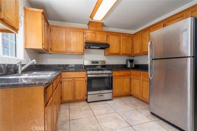 kitchen featuring light tile patterned floors, brown cabinetry, a sink, under cabinet range hood, and appliances with stainless steel finishes