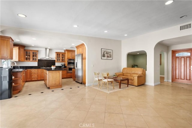 kitchen featuring visible vents, a sink, dark countertops, wall chimney exhaust hood, and a center island