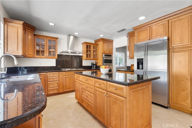 kitchen featuring dark stone countertops, a kitchen island, a sink, stainless steel appliances, and wall chimney range hood