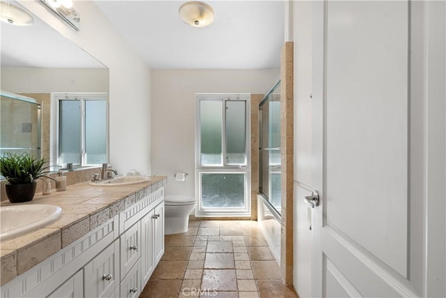 bathroom featuring double vanity, stone tile floors, toilet, and a sink