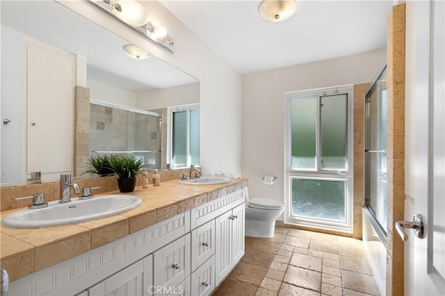 full bath with stone tile floors, toilet, a shower with door, and a sink