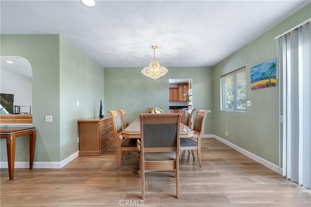 dining space with baseboards, arched walkways, a chandelier, and light wood finished floors