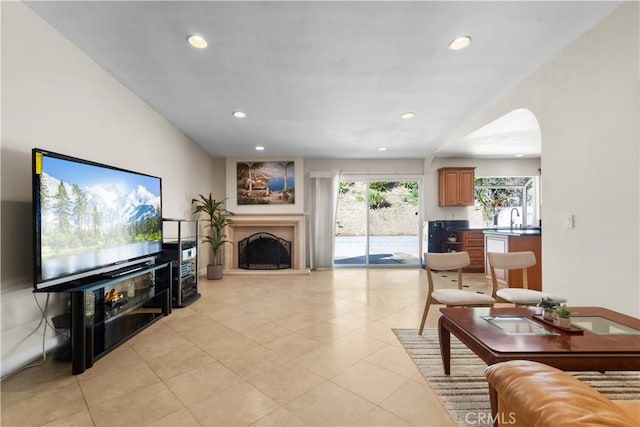 living room featuring light tile patterned floors, recessed lighting, a fireplace with raised hearth, and arched walkways