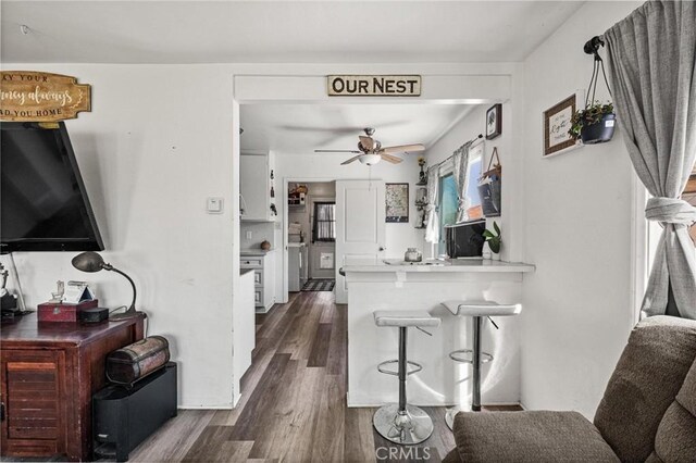 interior space featuring dark wood-type flooring, a breakfast bar, a peninsula, white cabinets, and a ceiling fan