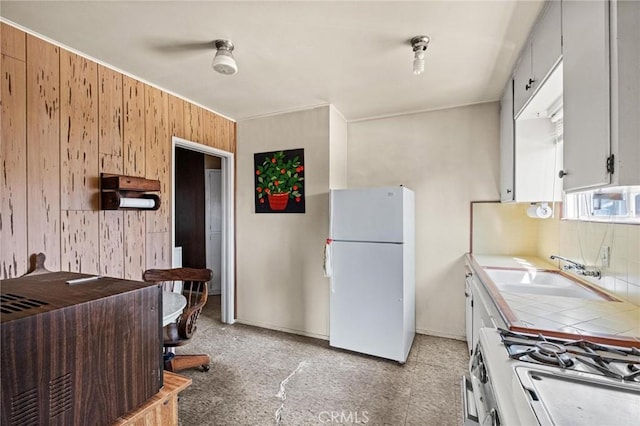 kitchen with backsplash, range with gas cooktop, tile countertops, freestanding refrigerator, and a sink