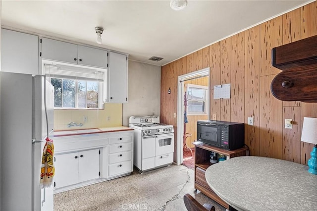 kitchen featuring visible vents, a sink, white appliances, wooden walls, and light countertops