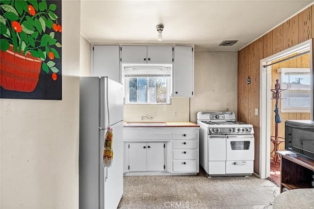 kitchen featuring visible vents, a sink, white appliances, wood walls, and light countertops