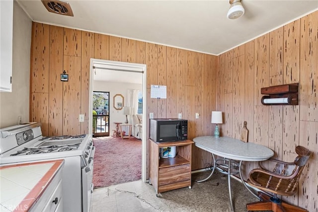 kitchen featuring gas range gas stove, tile countertops, white cabinets, black microwave, and light colored carpet