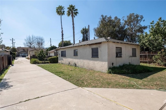 view of side of property featuring stucco siding, a lawn, a garage, and fence