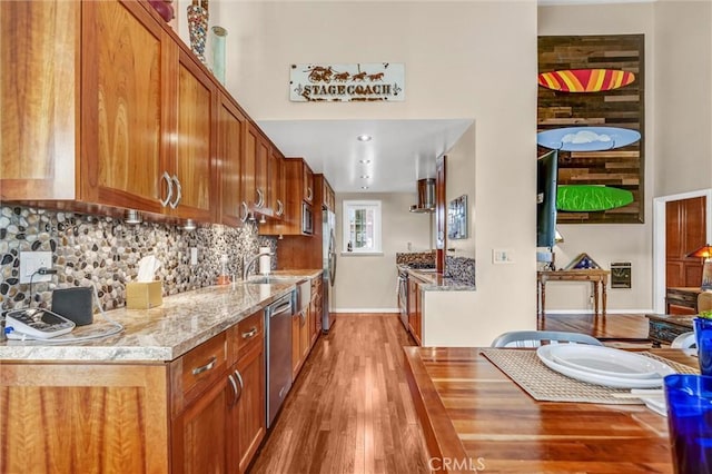 kitchen featuring light wood finished floors, backsplash, baseboards, brown cabinets, and appliances with stainless steel finishes