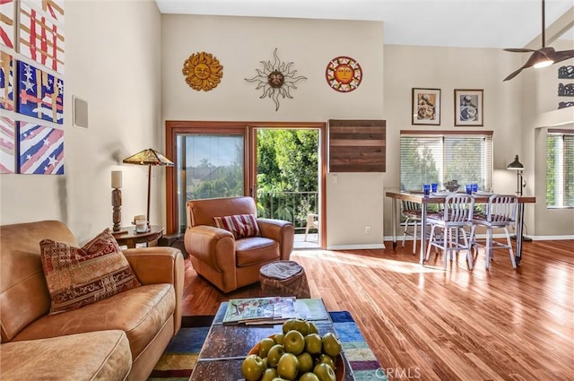 living room featuring ceiling fan, baseboards, a high ceiling, and wood finished floors