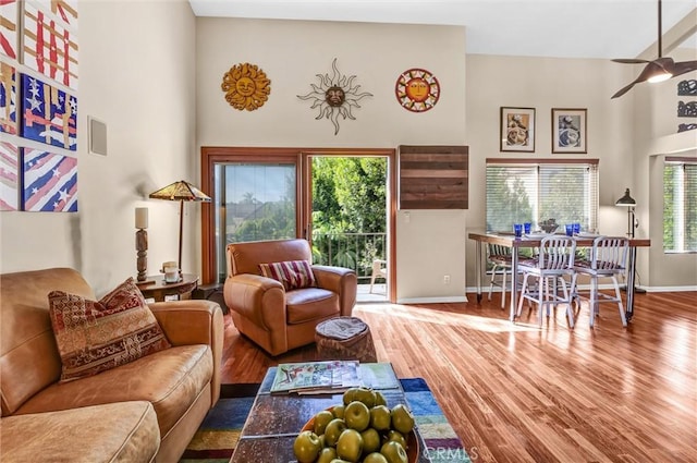 living room with ceiling fan, baseboards, wood finished floors, and a high ceiling