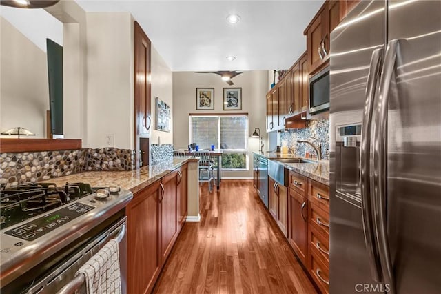 kitchen with dark wood finished floors, stone counters, decorative backsplash, appliances with stainless steel finishes, and a sink