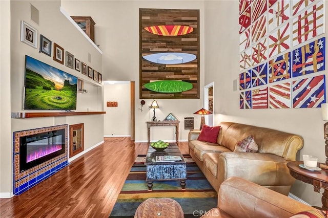 living area with a glass covered fireplace, baseboards, wood finished floors, and a towering ceiling