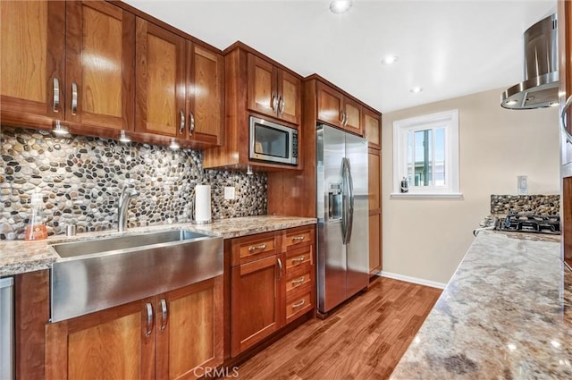 kitchen with brown cabinetry, a sink, light wood-style floors, appliances with stainless steel finishes, and tasteful backsplash