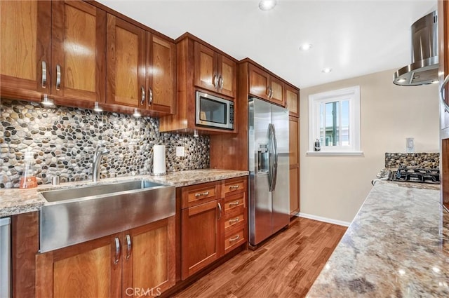 kitchen with brown cabinets, light wood finished floors, backsplash, a sink, and appliances with stainless steel finishes