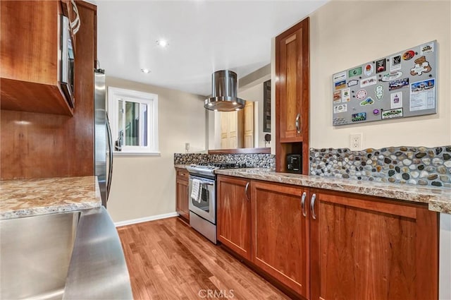 kitchen with brown cabinets, light wood-style flooring, tasteful backsplash, appliances with stainless steel finishes, and island range hood