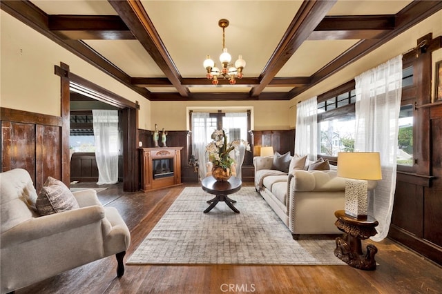 living area featuring wood finished floors, coffered ceiling, an inviting chandelier, beam ceiling, and a glass covered fireplace