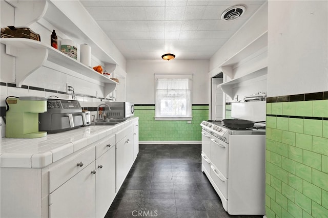 kitchen with a wainscoted wall, white range with electric cooktop, open shelves, a sink, and tile counters