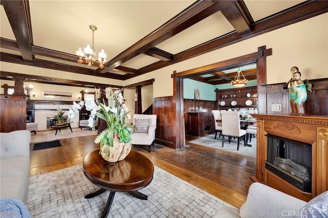 living area with a notable chandelier, wood finished floors, coffered ceiling, and wainscoting