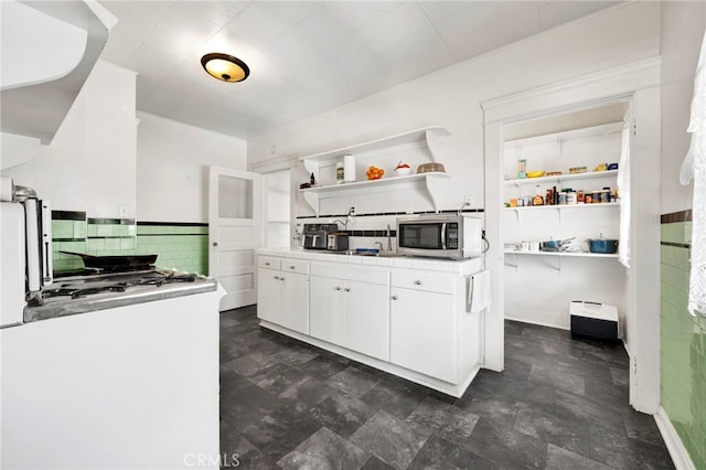 kitchen featuring stainless steel microwave, backsplash, tile countertops, white cabinets, and open shelves