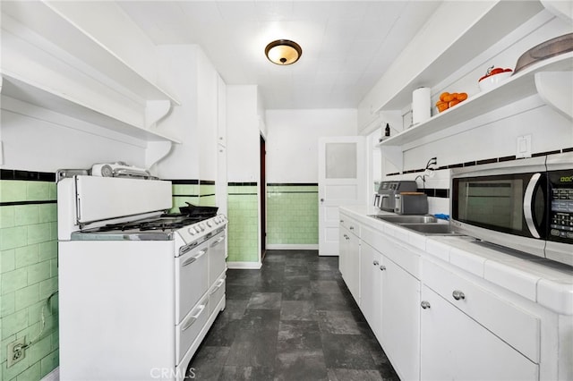 kitchen featuring a wainscoted wall, open shelves, stainless steel microwave, white gas range oven, and tile counters