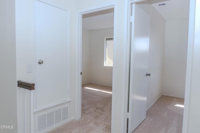 hall with visible vents, baseboards, and light colored carpet