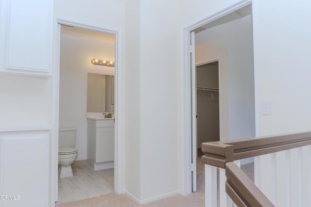 hallway featuring light colored carpet, baseboards, and a sink