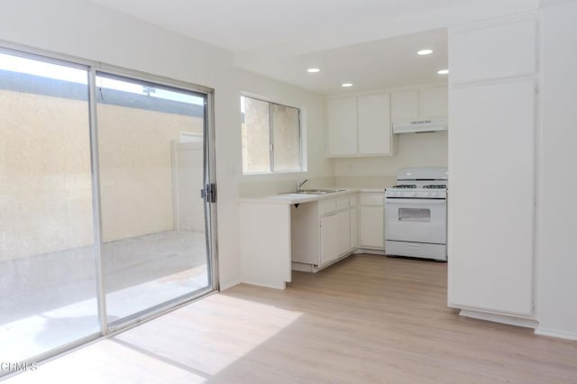 kitchen featuring light wood finished floors, a sink, light countertops, under cabinet range hood, and white gas range