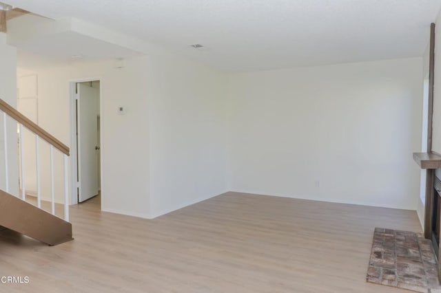 unfurnished living room with light wood-type flooring, stairs, and baseboards