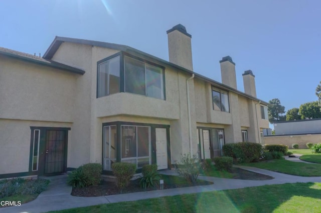 rear view of house with stucco siding, a lawn, and a chimney