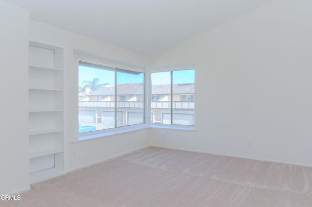 unfurnished room featuring built in features, baseboards, light carpet, and lofted ceiling