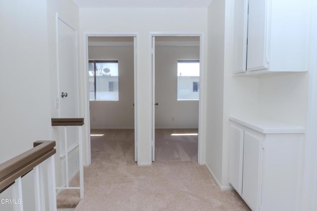 hall with a wealth of natural light, light colored carpet, and baseboards