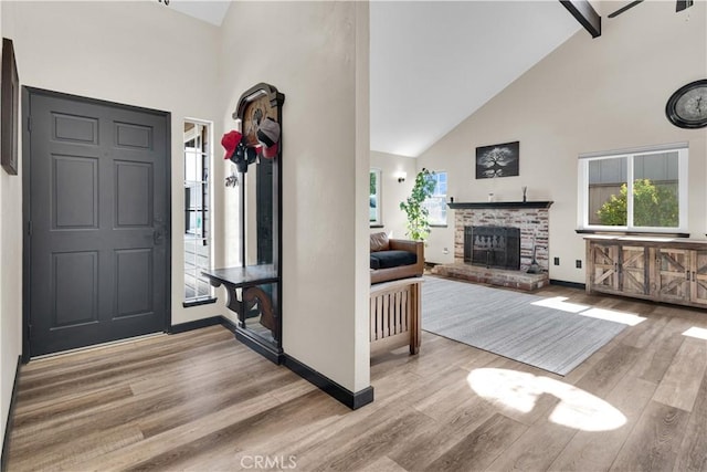 foyer entrance featuring beamed ceiling, a fireplace, light wood-type flooring, and high vaulted ceiling